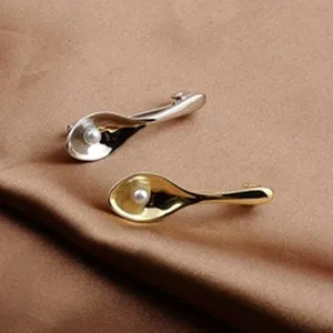 Primo piano dettagliato di spille a forma di cucchiaio color oro e argento con perle bianche.