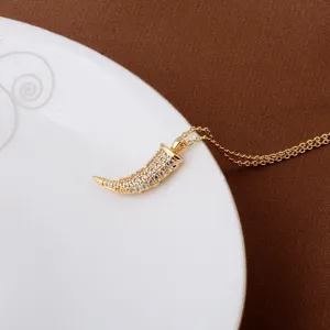 Close-up of 18K gold-plated tooth pendant necklace with micro-pave crystals on a white plate.