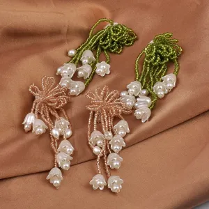 Detaillierte Nahaufnahme von Maiglöckchen-Ohrringen mit grünen und goldenen Perlenquasten.