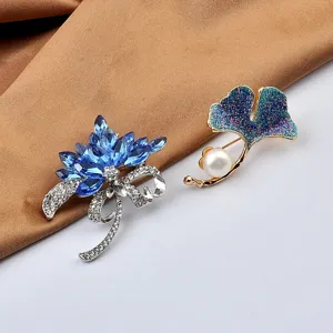 Nahaufnahme von eleganten Broschen mit blauen Kristallen und Ginkgoblatt-Perle auf Seide