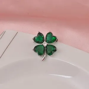 Dettaglio ravvicinato di una spilla argentata con pietre verdi sfaccettate a cuore.