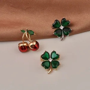 Dettaglio macro di eleganti spille a ciliegia e quadrifoglio verde con pietre dure