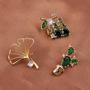 Close-up detail of gold plant brooches featuring ginkgo leaf and crystal cactus design