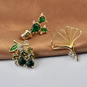 Close-up of elegant cactus, ginkgo, and berry plant brooches with green crystals.