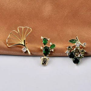 Close-up detail of golden ginkgo leaf, cactus, and grape brooches with green rhinestones