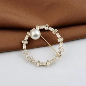 Nahaufnahme einer eleganten runden Brosche mit weißer Perle und Kristallen auf Goldbasis