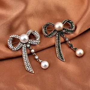 Close-up of elegant bow brooches with green and white rhinestones and pearls on satin fabric.