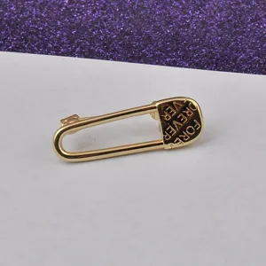 Detaillierte Nahaufnahme einer goldenen Sicherheitsnadel-Brosche mit "FOREVER"-Gravur.