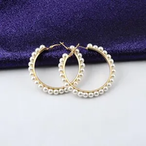 Primer plano de pendientes de aro dorados con elegantes adornos de perlas blancas
