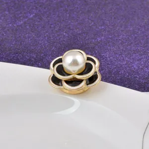 Macro detail of camellia magnetic brooch with pearl center and black enamel petals.