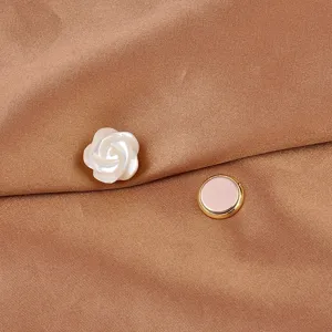 Primo piano di una spilla magnetica a forma di fiore di conchiglia su seta marrone.