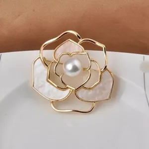 Detail view of a gold-tone camellia flower brooch with a central pearl accent