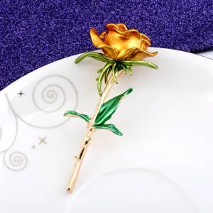 Detailaufnahme einer eleganten goldenen Rosenbrosche mit grünen Emaille-Blättern auf einem Teller.
