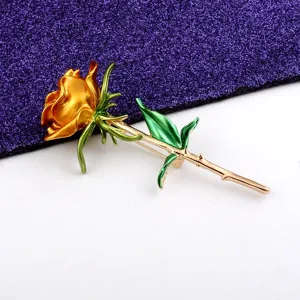 Nahaufnahme einer eleganten goldenen Rosenbrosche mit feinen Blütenblättern und grünen Blättern