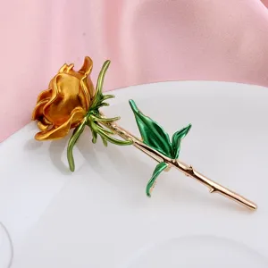 Detailansicht einer eleganten goldenen Rosenbrosche mit grünen Blättern