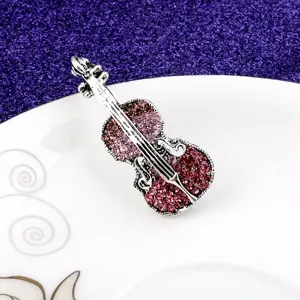 Close-up of vintage silver violin brooch adorned with pink rhinestones on a white plate