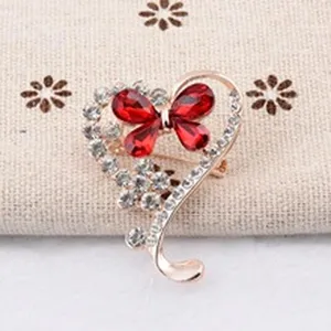 Détail d'une broche en cœur avec papillon en cristal rouge et de strass brillants