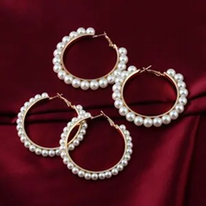 Elegante goldene Kreolen besetzt mit weißen Kunstperlen auf rotem Satinhintergrund