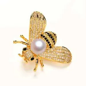 Detailansicht einer goldenen Bienenbrosche mit funkelnden Kristallen und großer weißer Perle