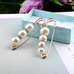 Detailansicht goldener Sicherheitsnadel-Brosche mit weißen Perlen und Strass.