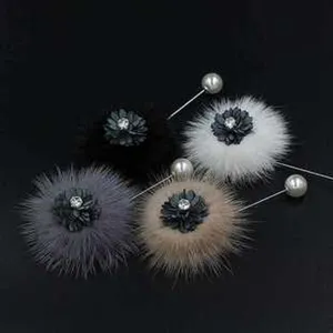 Detailansicht von Pelz-Pompon-Broschen mit Perlennadeln in Schwarz, Weiß und Grautönen.