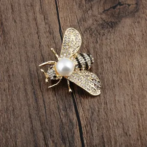 Nahaufnahme einer goldenen Bienennadel mit funkelnden Kristallen und Perlendetail