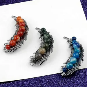 Detail view of feather brooches with colorful natural stone beads set on white card.