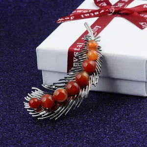 Close-up of a feather-shaped brooch with red natural stones on a white gift box