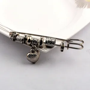 Detailed view of a retro silver heart brooch with intricate patterns on a safety pin
