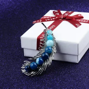Close-up of feather-shaped brooch with gradient blue natural stones on a gift box