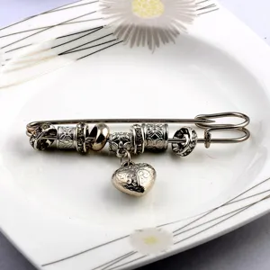 Vintage safety pin brooch with decorative beads and heart charm on a ceramic plate