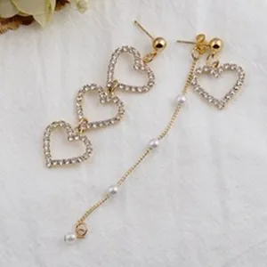 Elegante asymmetrische Goldohrringe mit glitzernden Herzchen und kleinen Perlen.