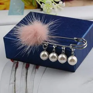 Detailansicht einer eleganten Brosche mit rosa Fellball und hängenden weißen Perlen.