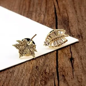 Nahaufnahme von goldenem Ahornblatt und Zirkon-Blatt-Reversnadeln auf Holzhintergrund