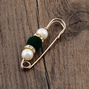 Detailed view of a gold safety pin brooch with white pearls and a green flocked bead.