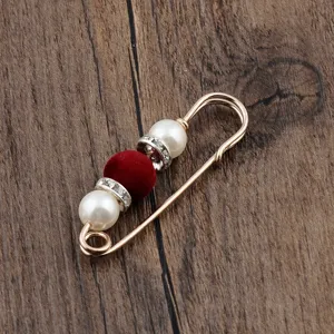 Detail view of an elegant safety pin brooch with red flocked bead and pearls.