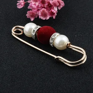 Detailed macro shot of a golden safety pin brooch with red velvet bead and white pearls