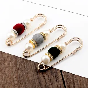 Close-up of three elegant safety pin brooches with pearls and colorful velvet beads