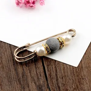 Close-up detail of decorative gold safety pin brooch with grey flocked bead and pearls