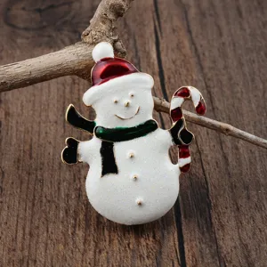 Detailansicht einer Emaille-Schneemann-Brosche mit Zuckerstange auf rustikalem Holzhintergrund