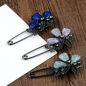 Detailweergave van drie elegante bloem- en esdoornbladbroches in blauwe en paarse tinten