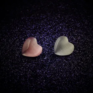 Detailansicht von rosa und weißen herzförmigen Katzenaugenstein-Broschen auf Glitzerhintergrund.
