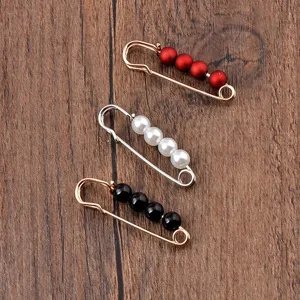 Vista macro de tres imperdibles decorativos con perlas rojas, blancas y negras sobre madera.