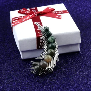 Detailed view of feather-shaped brooch with natural stone beads on a gift box