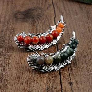 Detailed view of two feather brooches with natural red and green stones on wood background.