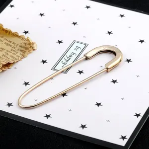 Close-up of a large gold-toned safety pin brooch displayed on a star-patterned card