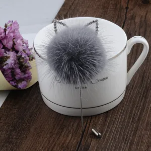 Detail einer grauen Nerzfell-Pompon-Brosche mit glitzernden Strass-Katzenohren und Nadel