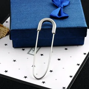 Close-up detail of a silver oversized safety pin brooch on a blue textured gift box.