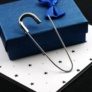 Detailed view of a large silver metal safety pin brooch on a blue jewelry gift box