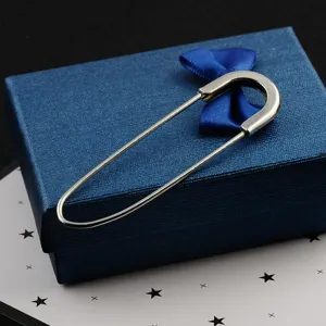 Detailed view of a large silver fashion safety pin brooch resting on a blue textured gift box